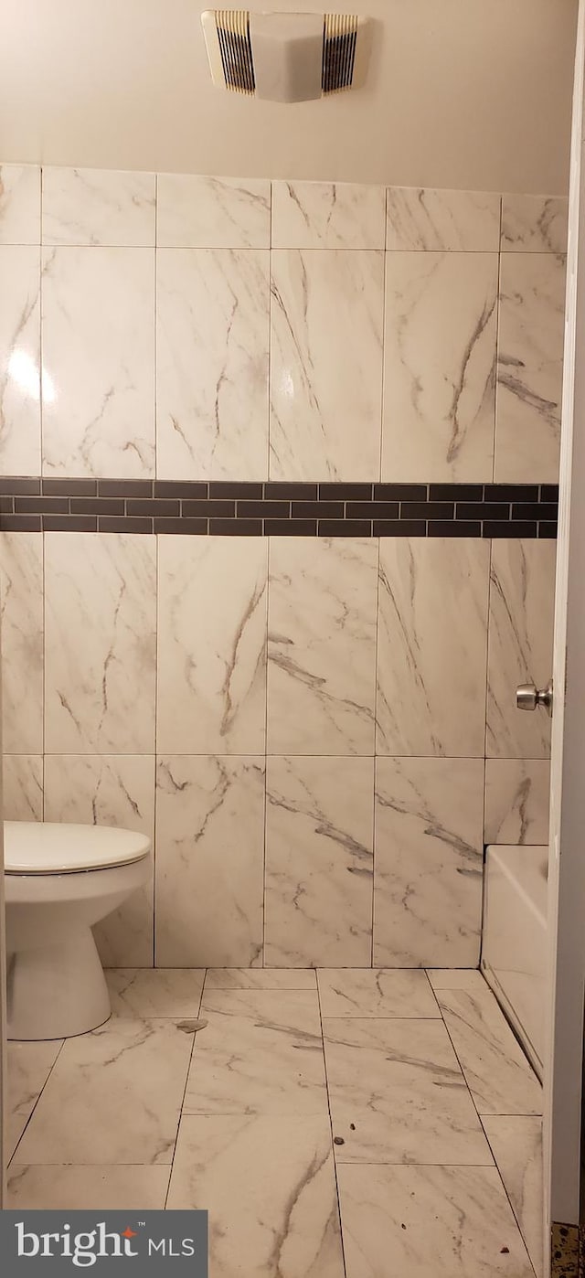 bathroom featuring toilet, tile flooring, and tile walls