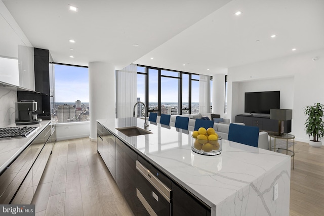 kitchen with a spacious island, sink, light hardwood / wood-style flooring, stainless steel gas cooktop, and light stone counters