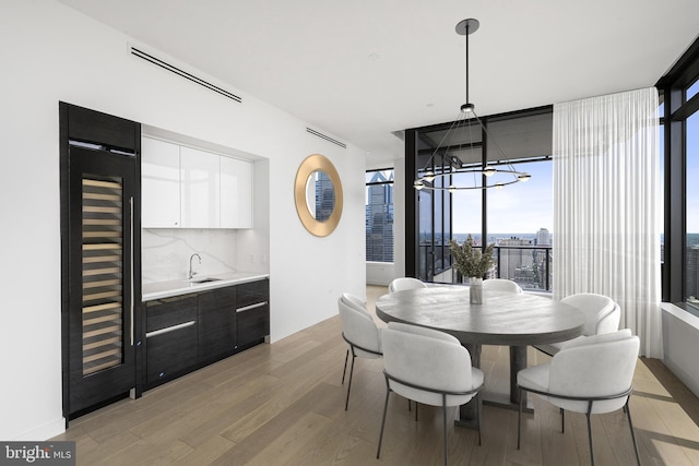 dining space featuring beverage cooler, a wall of windows, an inviting chandelier, sink, and light hardwood / wood-style flooring