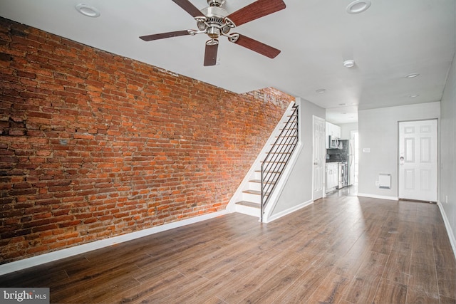 spare room with dark hardwood / wood-style flooring, ceiling fan, and brick wall