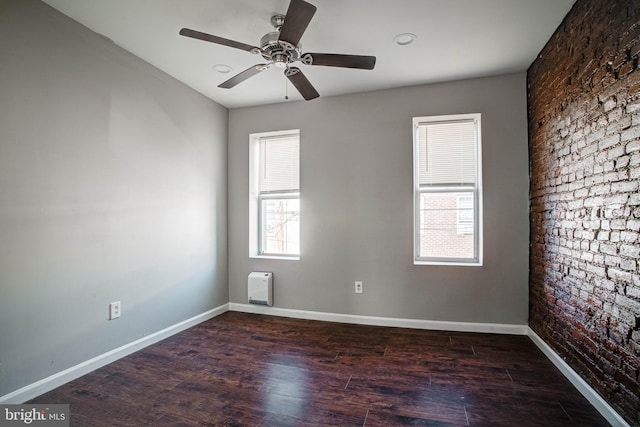 unfurnished room with dark hardwood / wood-style floors, ceiling fan, brick wall, and a wealth of natural light