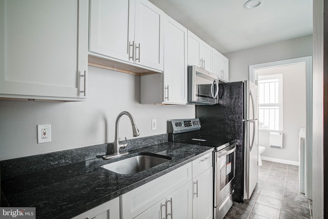 kitchen featuring sink, dark stone counters, white cabinets, appliances with stainless steel finishes, and light tile flooring