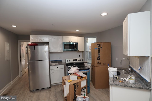 kitchen with appliances with stainless steel finishes, dark stone counters, light wood-type flooring, and white cabinets