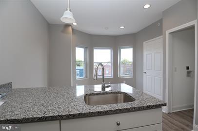 kitchen featuring dark hardwood / wood-style flooring, decorative light fixtures, light stone counters, white cabinetry, and sink