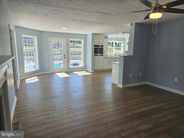 unfurnished living room featuring plenty of natural light, ceiling fan, and dark hardwood / wood-style flooring