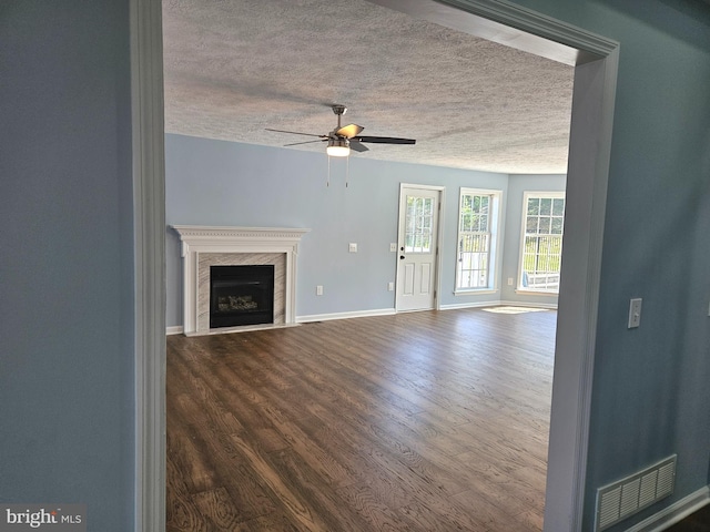 unfurnished living room with dark wood-type flooring, ceiling fan, a textured ceiling, and a fireplace