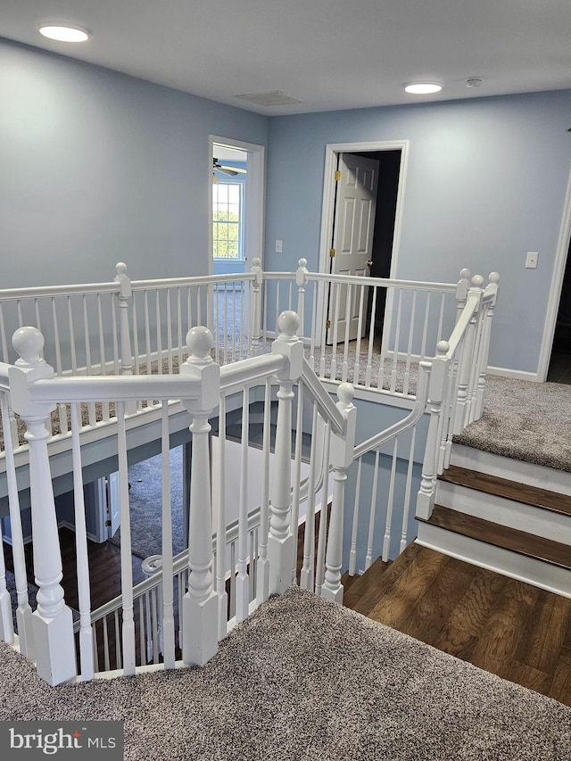 stairway with ceiling fan and dark colored carpet