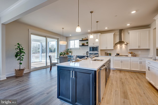 kitchen featuring pendant lighting, stainless steel microwave, light hardwood / wood-style floors, and wall chimney range hood