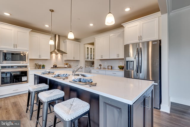 kitchen with hanging light fixtures, white cabinets, appliances with stainless steel finishes, and wall chimney exhaust hood