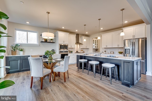 kitchen featuring white cabinets, wall chimney range hood, hanging light fixtures, and stainless steel appliances