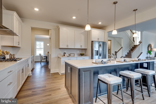 kitchen featuring white cabinets, a center island with sink, stainless steel appliances, light hardwood / wood-style flooring, and hanging light fixtures