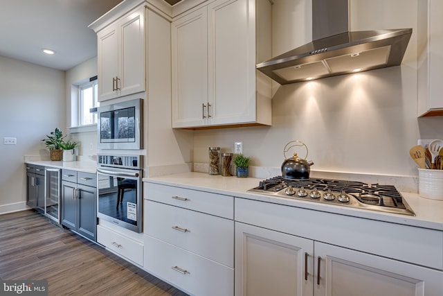 kitchen featuring light hardwood / wood-style floors, wall chimney range hood, wine cooler, appliances with stainless steel finishes, and white cabinets