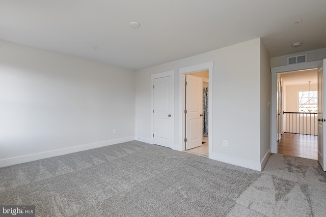 unfurnished bedroom with light colored carpet and a chandelier