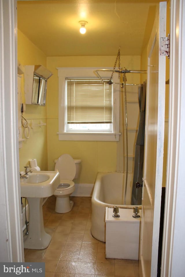 bathroom with a bath to relax in, tile floors, toilet, and a chandelier