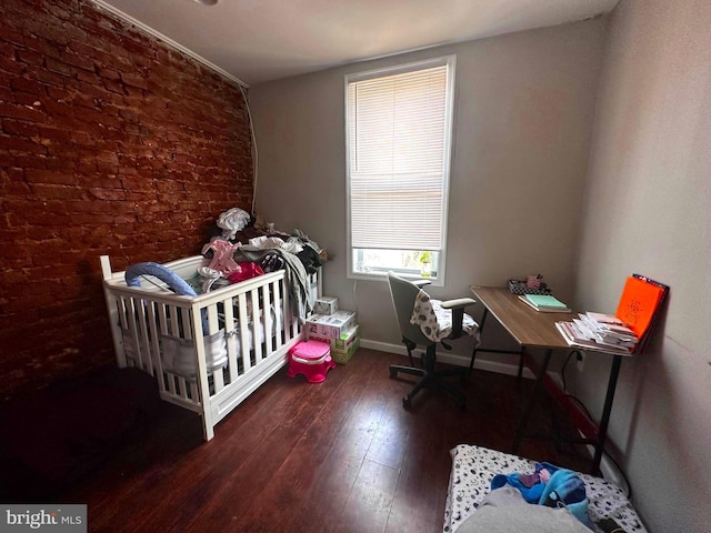 bedroom featuring brick wall, dark wood-type flooring, and a crib