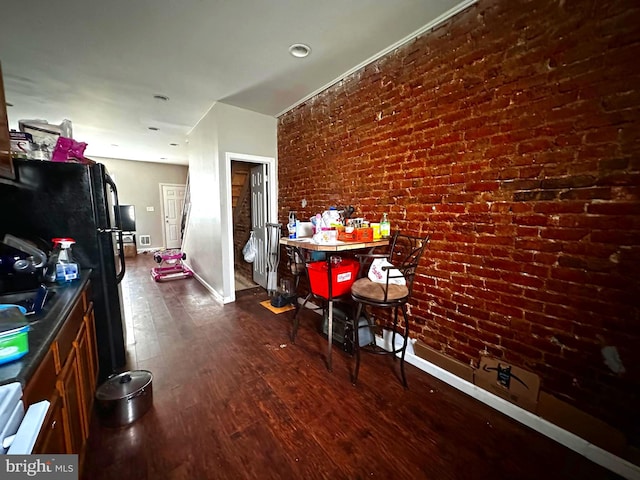 interior space featuring dark wood-type flooring, brick wall, and black refrigerator