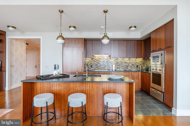 kitchen with an island with sink, dark tile floors, sink, hanging light fixtures, and stainless steel appliances