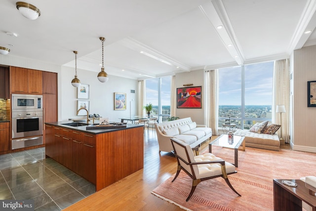 kitchen with decorative light fixtures, expansive windows, appliances with stainless steel finishes, sink, and an island with sink