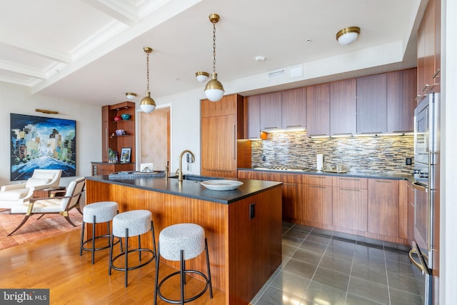 kitchen with an island with sink, sink, dark hardwood / wood-style flooring, decorative light fixtures, and a kitchen bar