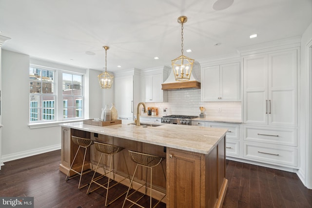 kitchen featuring custom exhaust hood, dark hardwood / wood-style flooring, white cabinetry, light stone countertops, and a center island with sink