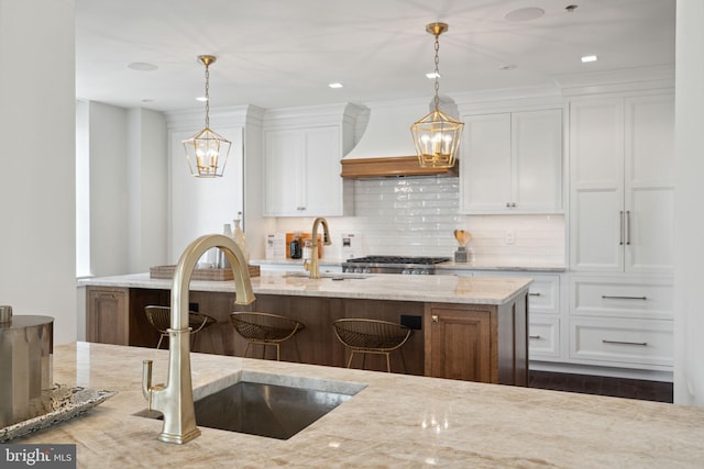 kitchen featuring white cabinetry, tasteful backsplash, premium range hood, and light stone countertops