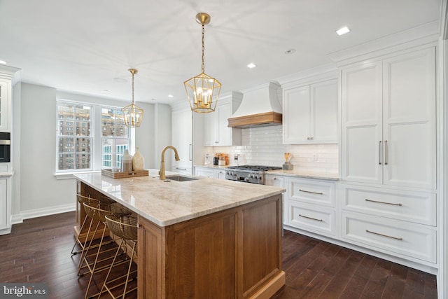 kitchen with an island with sink, white cabinetry, sink, and premium range hood