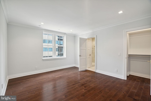 unfurnished bedroom featuring a spacious closet, ornamental molding, a closet, and dark wood-type flooring