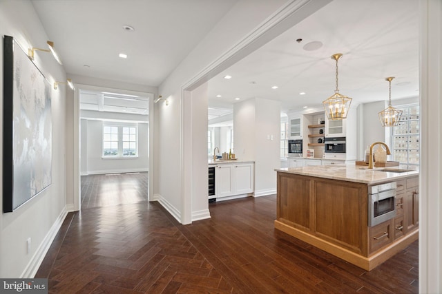 kitchen with light stone countertops, hanging light fixtures, sink, an island with sink, and wine cooler