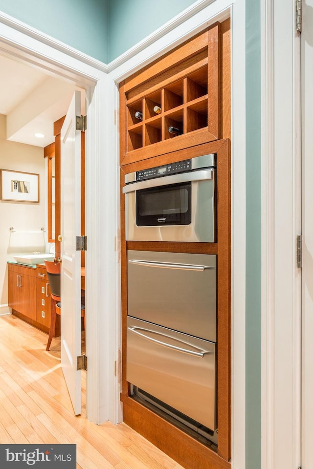 interior details featuring stainless steel oven, built in desk, and light hardwood / wood-style floors