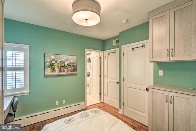 bedroom featuring a baseboard radiator, stacked washer and dryer, and light hardwood / wood-style flooring