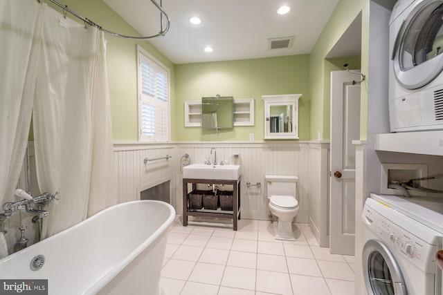 bathroom featuring toilet, stacked washer / dryer, tile floors, and sink