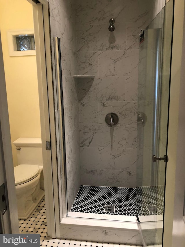 bathroom with toilet, tiled shower, and tile floors