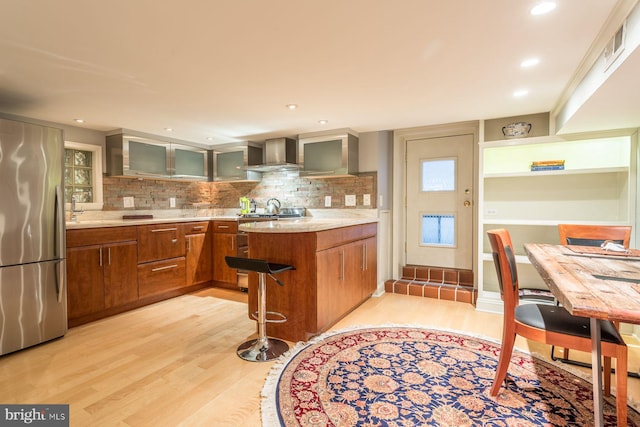 kitchen with stainless steel refrigerator, light hardwood / wood-style flooring, tasteful backsplash, and wall chimney exhaust hood