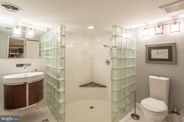 bathroom featuring vanity, tile walls, a tile shower, tile flooring, and toilet