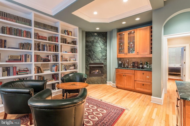 living area with built in shelves, a tray ceiling, a high end fireplace, and light hardwood / wood-style floors