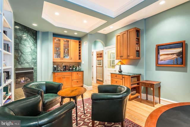 interior space featuring crown molding, a raised ceiling, a premium fireplace, and light hardwood / wood-style floors