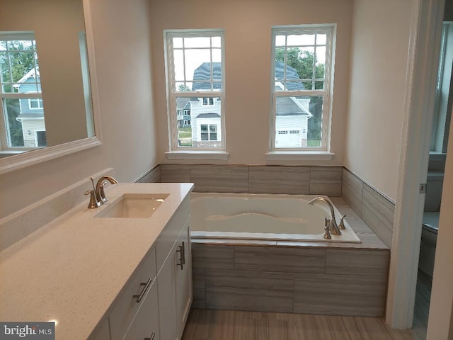 bathroom featuring vanity, a healthy amount of sunlight, and tiled bath