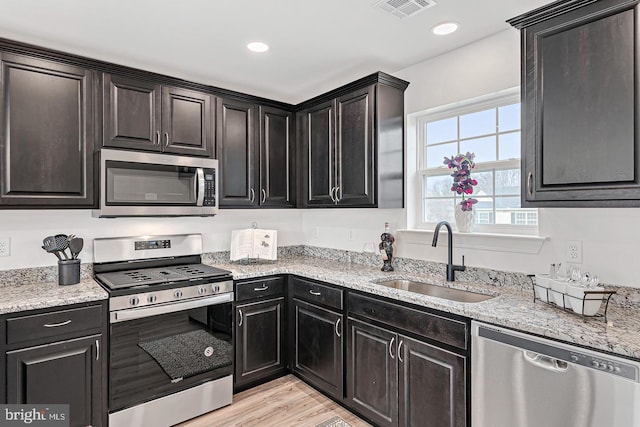 kitchen with sink, light wood-type flooring, stainless steel appliances, and light stone countertops