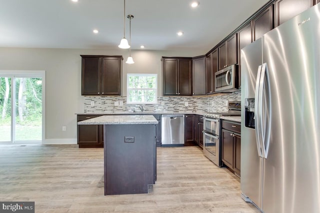 kitchen with decorative light fixtures, stainless steel appliances, light stone counters, a kitchen island, and tasteful backsplash