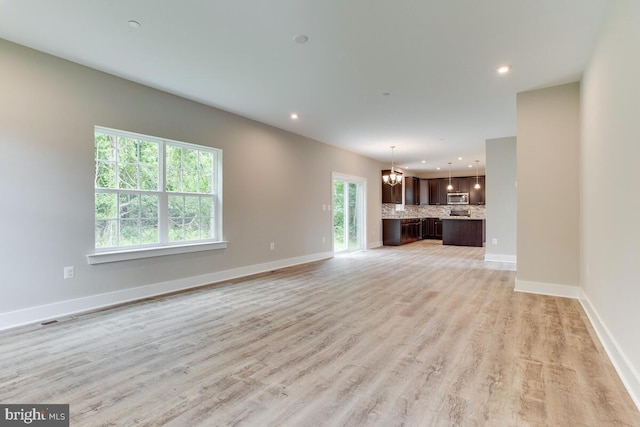 unfurnished living room with an inviting chandelier and light hardwood / wood-style floors