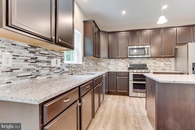 kitchen featuring light wood-type flooring, tasteful backsplash, decorative light fixtures, and appliances with stainless steel finishes