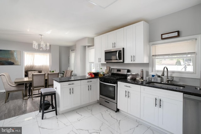 kitchen featuring appliances with stainless steel finishes, decorative light fixtures, sink, white cabinetry, and a chandelier