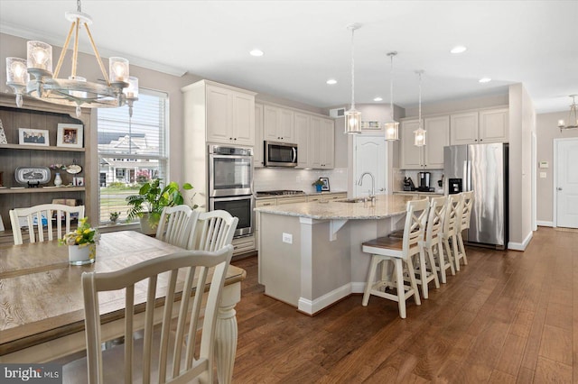 kitchen featuring an island with sink, hanging light fixtures, appliances with stainless steel finishes, and a breakfast bar