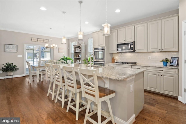 kitchen featuring dark hardwood / wood-style floors, an inviting chandelier, appliances with stainless steel finishes, an island with sink, and pendant lighting