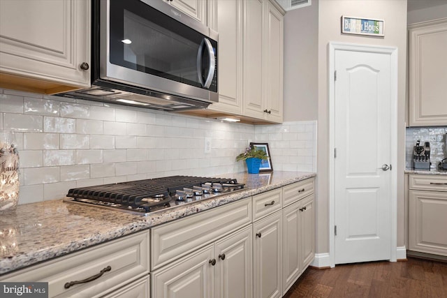 kitchen with dark hardwood / wood-style flooring, tasteful backsplash, stainless steel appliances, and light stone countertops