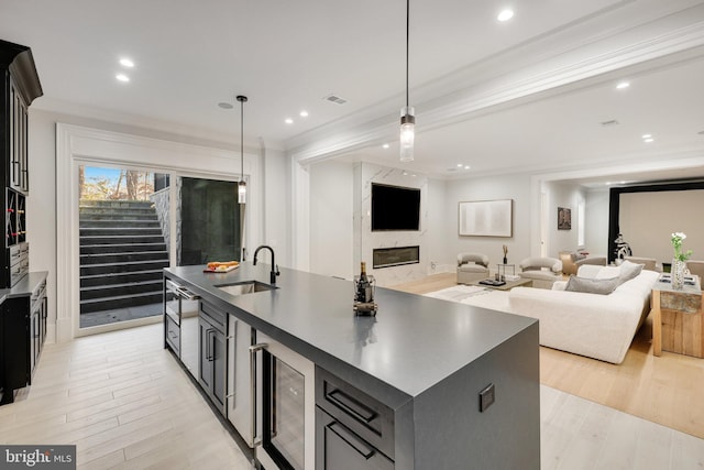 kitchen with pendant lighting, a kitchen island with sink, ornamental molding, and sink