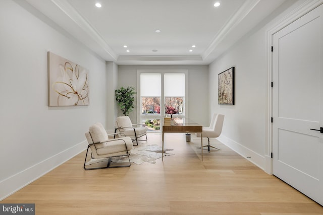 sitting room with light hardwood / wood-style floors, a raised ceiling, and ornamental molding