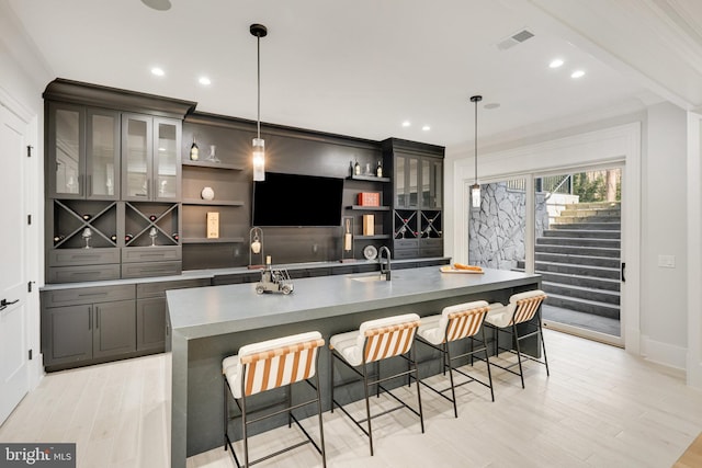 kitchen featuring light wood-type flooring, ornamental molding, a breakfast bar, a center island with sink, and hanging light fixtures