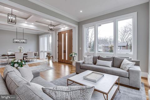 living room with light wood-type flooring, ornamental molding, and coffered ceiling