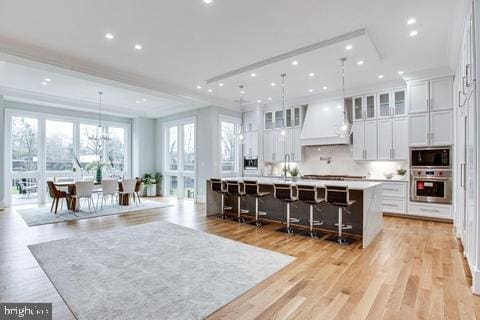 kitchen with a kitchen breakfast bar, oven, custom range hood, a large island, and white cabinetry